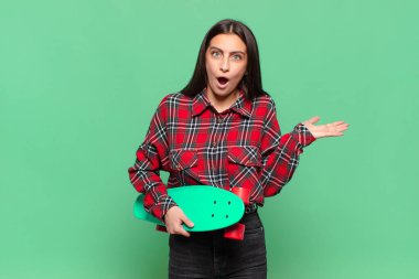 Genç ve güzel bir kadın şaşırmış ve şok olmuş görünüyor. Çenesi düşmüş ve eli açık bir objeyi tutuyor. kaykay konsepti