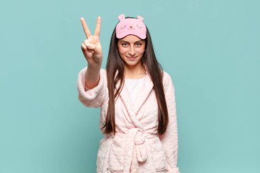 Genç, güzel bir kadın gülümsüyor ve arkadaş canlısı görünüyor. İki ya da iki numarayı gösteriyor. Elleri önde, geriye doğru sayıyor. Pijama giyip uyanmak