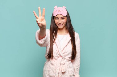 Genç, güzel bir bayan gülümsüyor ve arkadaş canlısı görünüyor. Üç ya da üç numarayı gösteriyor. Elleri önde, geriye doğru sayıyor. Pijama giyip uyanmak