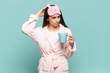 Genç, güzel bir kadın şaşkın ve kafası karışmış hissediyor. Kafasını kaşıyor ve yan tarafa bakıyor. Pijama giyip uyanmak