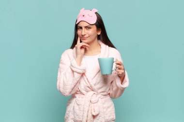 Genç ve güzel bir kadın mutlu bir şekilde gülümsüyor ve hayal kuruyor ya da şüphe ediyor, yan tarafa bakıyor. Pijama giyip uyanmak