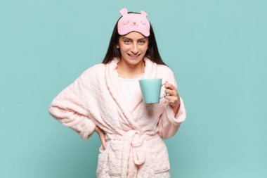 Genç ve güzel bir kadın mutlu bir şekilde gülümsüyor, eli kalçasında ve kendinden emin, olumlu, gururlu ve arkadaş canlısı bir tavırla. Pijama giyip uyanmak