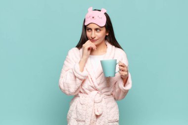 Genç, güzel bir kadın, mutlu, kendinden emin bir ifadeyle gülümsüyor, elleri çenesinde, merak ediyor ve yan tarafa bakıyor. Pijama giyip uyanmak