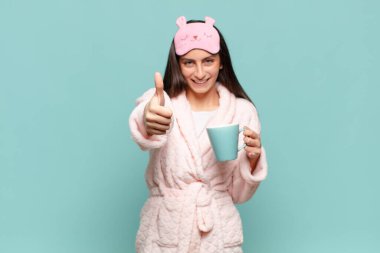 Genç, güzel bir kadın gururlu, tasasız, kendinden emin ve mutlu, başparmağıyla olumlu gülümsüyor. Pijama giyip uyanmak