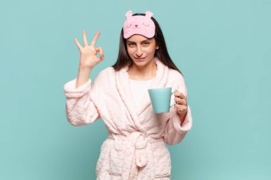 Genç, güzel bir kadın kendini mutlu, rahat ve tatmin olmuş hissediyor. İyi bir jestle onaylıyor, gülümsüyor. Pijama giyip uyanmak