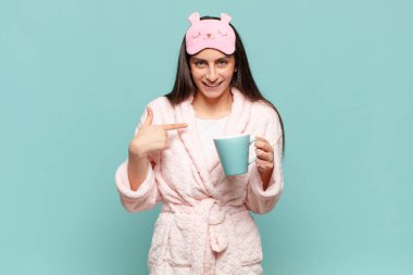 Genç, güzel bir kadın mutlu, şaşırmış ve gururlu hissediyor. Heyecanlı ve şaşkın bir bakışla kendini işaret ediyor. Pijama giyip uyanmak