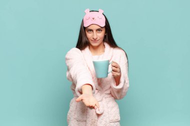 Genç, güzel bir kadın mutlu bir şekilde gülümsüyor. Dost canlısı, kendine güvenen, olumlu bakışlı, bir nesne ya da konsept sunuyor. Pijama giyip uyanmak