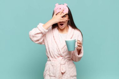 Genç, güzel bir kadın şok olmuş, korkmuş ya da korkmuş görünüyor. Yüzü elle kaplanmış ve parmaklarının arasından gizlice bakıyor. Pijama giyip uyanmak