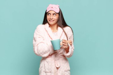 Genç, güzel bir kadın omuz silkiyor, kafası karışık ve kararsız, kolları bağlı ve şaşkın görünüyor. Pijama giyip uyanmak