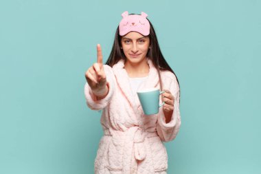 Genç ve güzel bir kadın gülümsüyor ve arkadaş canlısı görünüyor. Bir numarayı gösteriyor ya da ilk eli önde, geri sayıyor. Pijama giyip uyanmak