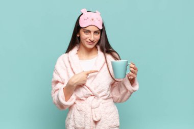 Genç, güzel bir kadın neşeyle gülümsüyor, mutlu hissediyor ve yan ve yukarı doğru işaret ediyor, fotokopi uzayında nesneler gösteriyor. Pijama giyip uyanmak