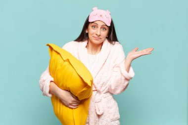 Genç ve güzel bir kadın şaşkın ve şaşkın hissediyor, şüpheci, farklı seçenekleri tartıyor ya da komik bir ifadeyle seçiyor. Pijama giyip uyanmak