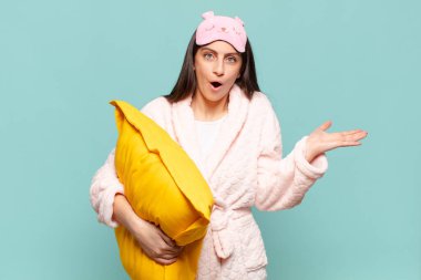 Genç ve güzel bir kadın şaşırmış ve şok olmuş görünüyor. Çenesi düşmüş ve eli açık bir objeyi tutuyor. Pijama giyip uyanmak