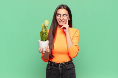 Genç ve güzel bir kadın mutlu bir şekilde gülümsüyor ve hayal kuruyor ya da şüphe ediyor, yan tarafa bakıyor. Kaktüs kavramı