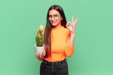 Genç, güzel bir kadın kendini mutlu, rahat ve tatmin olmuş hissediyor. İyi bir jestle onaylıyor, gülümsüyor. Kaktüs kavramı