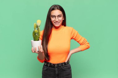 Genç ve güzel bir kadın mutlu bir şekilde gülümsüyor, eli kalçasında ve kendinden emin, olumlu, gururlu ve arkadaş canlısı bir tavırla. Kaktüs kavramı