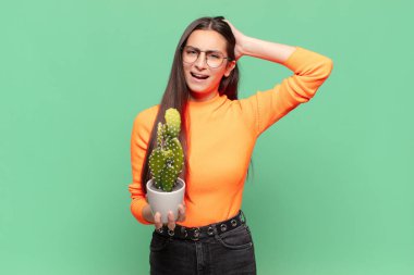 Genç, güzel bir kadın kendini stresli, endişeli, endişeli ya da korkmuş hissediyor. Elleri başının üstünde, hatayla panikliyor. Kaktüs kavramı