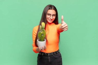 Genç, güzel bir kadın gururlu, tasasız, kendinden emin ve mutlu, başparmağıyla olumlu gülümsüyor. Kaktüs kavramı