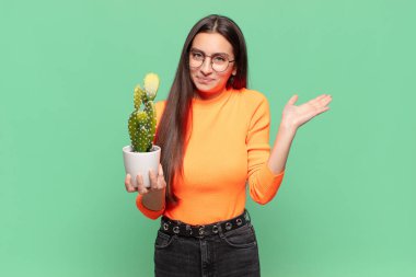 Genç ve güzel bir kadın şaşkın ve şaşkın hissediyor, şüpheci, farklı seçenekleri tartıyor ya da komik bir ifadeyle seçiyor. Kaktüs kavramı