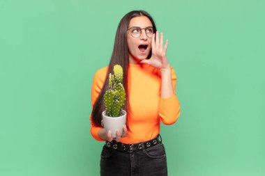 Genç, güzel bir kadın mutlu, heyecanlı ve pozitif hissediyor. Elleri ağızda, bağırarak bağırıyor. Kaktüs kavramı