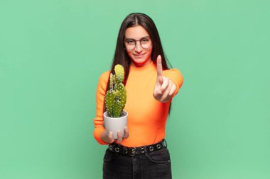 Genç ve güzel bir kadın gururla gülümsüyor ve gururla bir numaralı pozunu veriyor, bir lider gibi hissediyor. Kaktüs kavramı