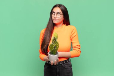 Genç, güzel bir kadın omuz silkiyor, kafası karışık ve kararsız, kolları bağlı ve şaşkın görünüyor. Kaktüs kavramı