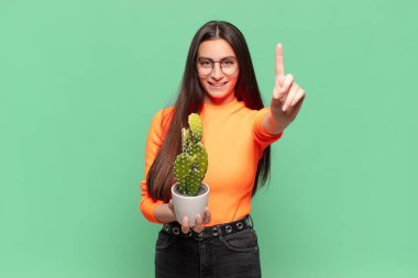 Genç ve güzel bir kadın gülümsüyor ve arkadaş canlısı görünüyor. Bir numarayı gösteriyor ya da ilk eli önde, geri sayıyor. Kaktüs kavramı