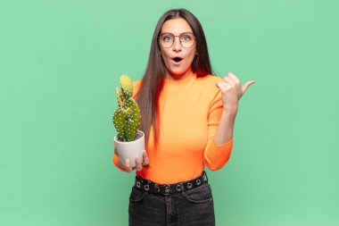 Genç ve güzel bir kadın inançsızlıktan şaşkın şaşkın bakıyor, yan taraftaki objeyi işaret ediyor ve 