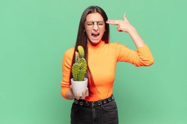 Genç ve güzel bir kadın mutsuz ve stresli görünüyor, intihar jesti, silahla işaret ediyor, kafasını işaret ediyor. Kaktüs kavramı