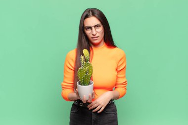 young pretty woman feeling puzzled and confused, with a dumb, stunned expression looking at something unexpected. cactus concept