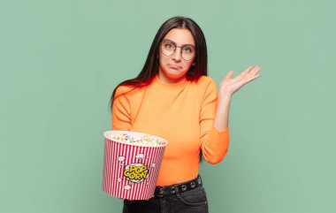 Genç ve güzel bir kadın şaşkın ve şaşkın hissediyor, şüpheci, farklı seçenekleri tartıyor ya da komik bir ifadeyle seçiyor. patlamış mısır konsepti