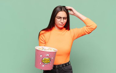 Genç, güzel bir kadın şaşkın ve kafası karışmış hissediyor. Kafasını kaşıyor ve yan tarafa bakıyor. patlamış mısır konsepti