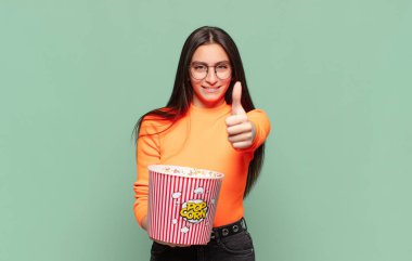 Genç, güzel bir kadın gururlu, tasasız, kendinden emin ve mutlu, başparmağıyla olumlu gülümsüyor. patlamış mısır konsepti