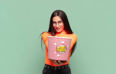 Genç, güzel bir kadın mutlu bir şekilde gülümsüyor. Dost canlısı, kendine güvenen, olumlu bakışlı, bir nesne ya da konsept sunuyor. patlamış mısır konsepti