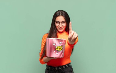 Genç ve güzel bir kadın gülümsüyor ve arkadaş canlısı görünüyor. Bir numarayı gösteriyor ya da ilk eli önde, geri sayıyor. patlamış mısır konsepti