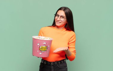 Genç, güzel bir kadın neşeyle gülümsüyor, mutlu hissediyor ve fotokopi uzayda avucuyla bir konsept gösteriyor. patlamış mısır konsepti