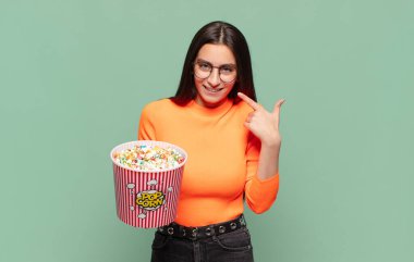 Genç, güzel bir kadın, kendine güvenerek gülümsüyor. Geniş bir gülümseme, pozitif, rahat, tatmin olmuş bir tavır sergiliyor. patlamış mısır konsepti