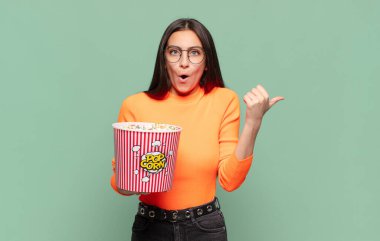 Genç ve güzel bir kadın inançsızlıktan şaşkın şaşkın bakıyor, yan taraftaki objeyi işaret ediyor ve 