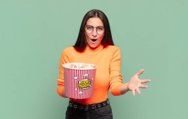 Genç ve güzel bir kadın ağzı açık ve şaşırmış, şok olmuş ve hayrete düşmüş inanılmaz bir sürprizle. patlamış mısır konsepti