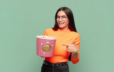 Genç ve güzel bir kadın heyecanlı ve şaşırmış görünüyor. Yana ve yukarı doğru uzayı işaret ediyor. patlamış mısır konsepti