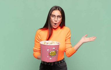 Genç ve güzel bir kadın şaşırmış ve şok olmuş görünüyor. Çenesi düşmüş ve eli açık bir objeyi tutuyor. patlamış mısır konsepti
