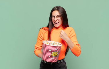 Genç ve güzel bir kadın öfkeli bir ifadeyle ya da yumruklarıyla başarıyı kutlarken agresif bir şekilde bağırıyor. patlamış mısır konsepti