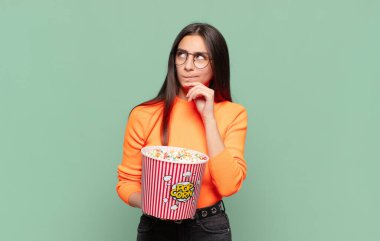 Genç, güzel bir kadın düşünüyor, kuşkulu ve şaşkın hissediyor, farklı seçeneklerle, hangi kararı vereceğini merak ediyor. patlamış mısır konsepti