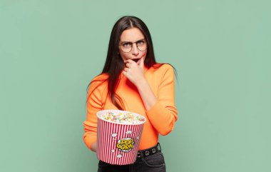 Ağzı ve gözleri açık, eli çenesinde genç ve güzel bir kadın. Hoş olmayan bir şok geçiriyor. Ne diyor? patlamış mısır konsepti