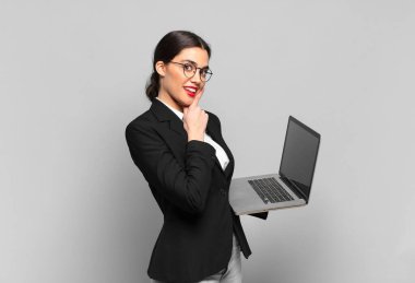 Genç ve güzel bir kadın mutlu bir şekilde gülümsüyor ve hayal kuruyor ya da şüphe ediyor, yan tarafa bakıyor. dizüstü bilgisayar