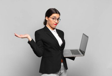 Genç ve güzel bir kadın şaşkın ve şaşkın hissediyor, şüpheci, farklı seçenekleri tartıyor ya da komik bir ifadeyle seçiyor. dizüstü bilgisayar