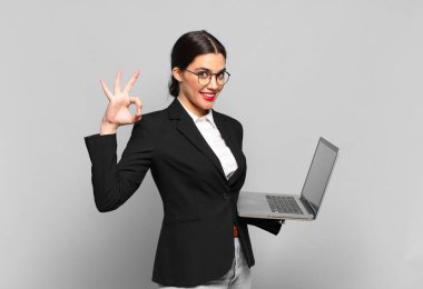 Genç, güzel bir kadın kendini mutlu, rahat ve tatmin olmuş hissediyor. İyi bir jestle onaylıyor, gülümsüyor. dizüstü bilgisayar