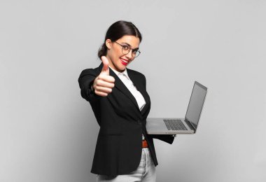 Genç, güzel bir kadın gururlu, tasasız, kendinden emin ve mutlu, başparmağıyla olumlu gülümsüyor. dizüstü bilgisayar