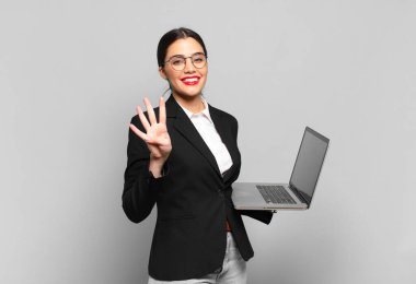 Genç, güzel bir bayan gülümsüyor ve arkadaş canlısı görünüyor. Dört ya da dört numarayı gösteriyor. Elleri önde ve geri sayıyor. dizüstü bilgisayar