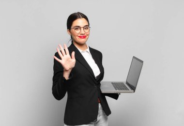 Genç ve güzel bir bayan gülümsüyor ve arkadaş canlısı görünüyor. Beş ya da beş numarayı gösteriyor. Elleri önde ve geri sayıyor. dizüstü bilgisayar